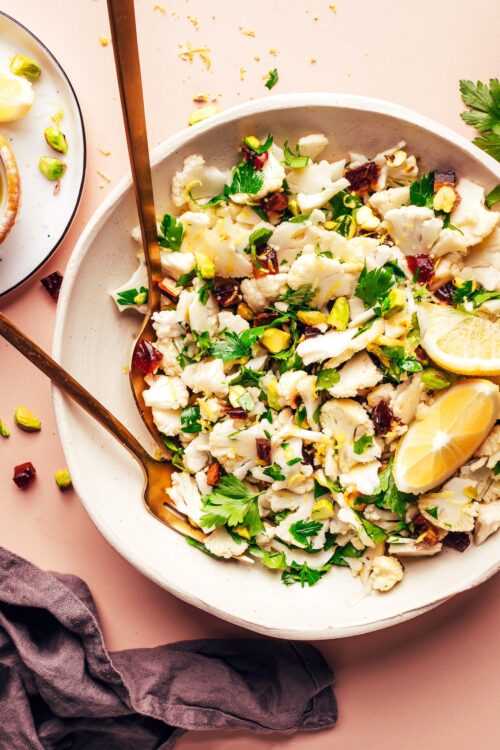 Fork and spoon resting in a bowl of our easy raw chopped cauliflower salad