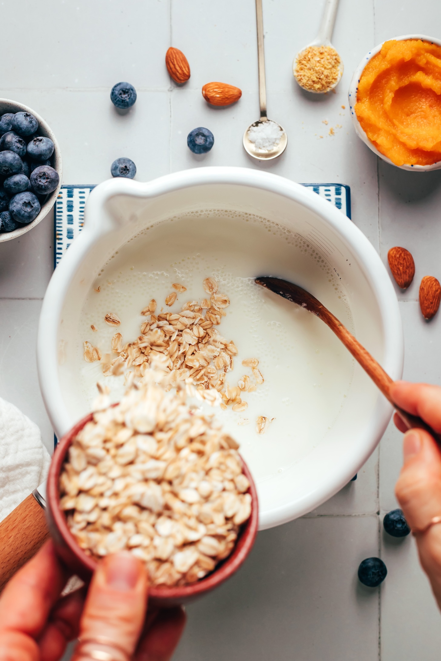 Pouring rolled oats into a saucepan of  warmed almond milk