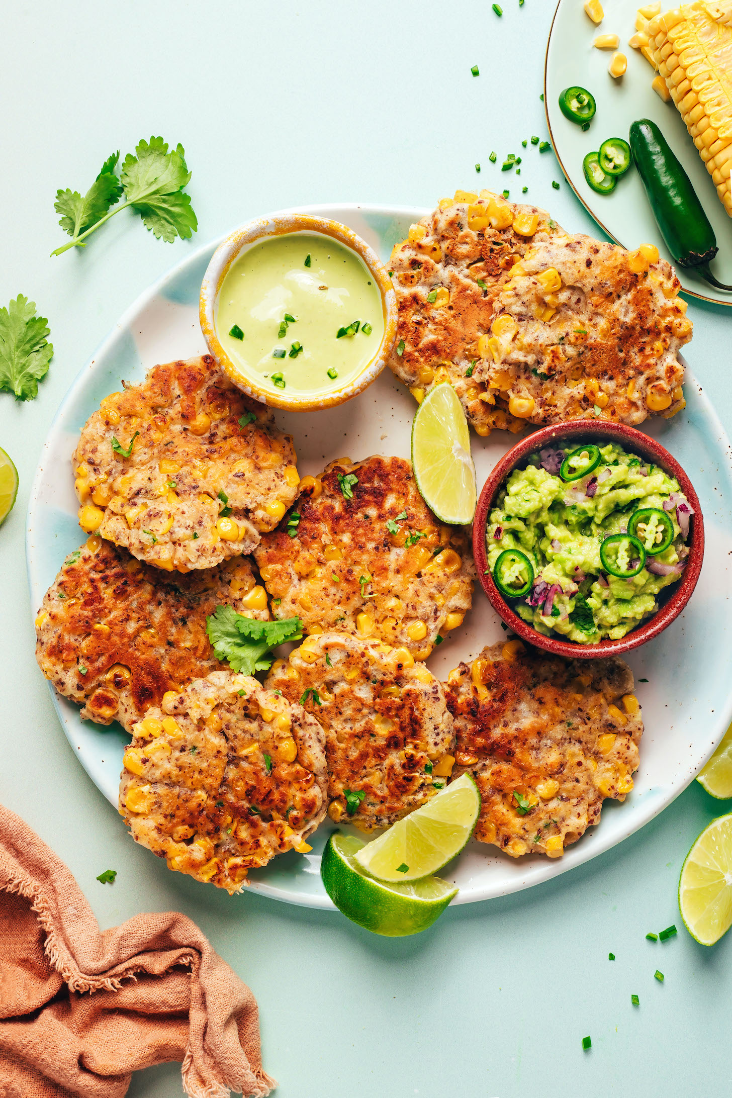 Plate of vegan corn fritters with lime wedges and two small bowls of dips