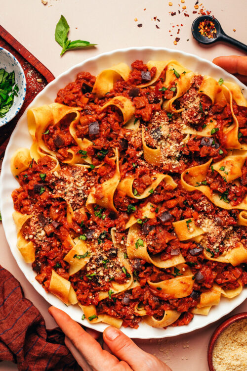 Hands holding the sides of a large plate of our vegan eggplant bolognese